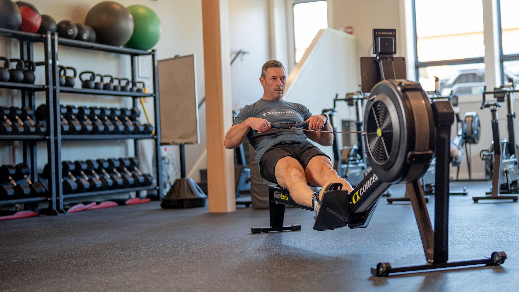 Man rowing on Concept2 RowErg with weights in the background